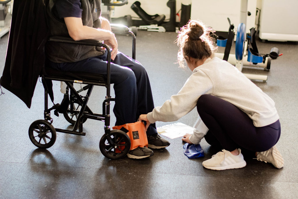 A student volunteer helping a program member with exercise equipment at Revved Up